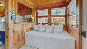 A wooden cabin bedroom with a bed, pillows, a hanging bat, and a window with a view. - Charming cottage with private W/D, wifi + minutes to beach (Dennis)