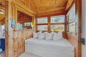 A wooden cabin bedroom with a bed, pillows, a hanging bat, and a window with a view.
