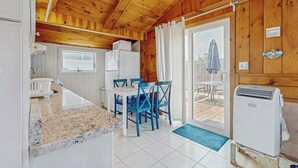 A wooden interior with a kitchen, dining area, and a sliding glass door leading to an outdoor patio. - Charming cottage with private W/D, wifi + minutes to beach (Dennis)