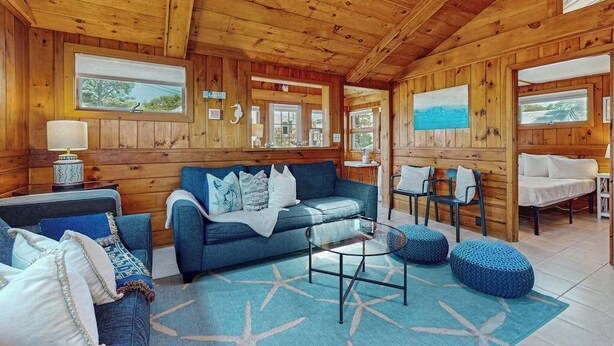 A wooden cabin interior with a sofa, chairs, a small table, and a rug. - Charming cottage with private W/D, wifi + minutes to beach (Dennis)