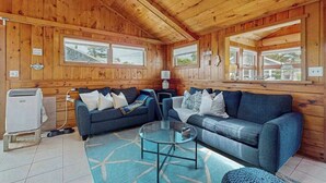 A wooden cabin interior with two sofas, a glass coffee table, and a heater. - Charming cottage with private W/D, wifi + minutes to beach (Dennis)