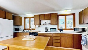 Uma cozinha com armários de madeira, bancada branca, forno embutido, micro-ondas e janela com vista.