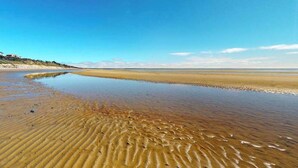 Uma praia com águas claras, areal arenoso e um prédio ao longe.