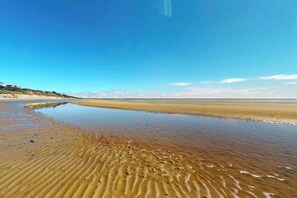 A beach with clear water, a sandy shore, and a distant building.