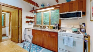 A kitchen with wooden cabinets, a microwave, a stove, and a window with a view of greenery.