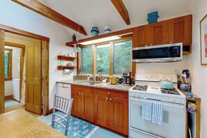 A kitchen with wooden cabinets, a microwave, a stove, and a window with a view of greenery. - Peaceful, dog-friendly home on 3 acres with lovely yard, near beaches (Chilmark)