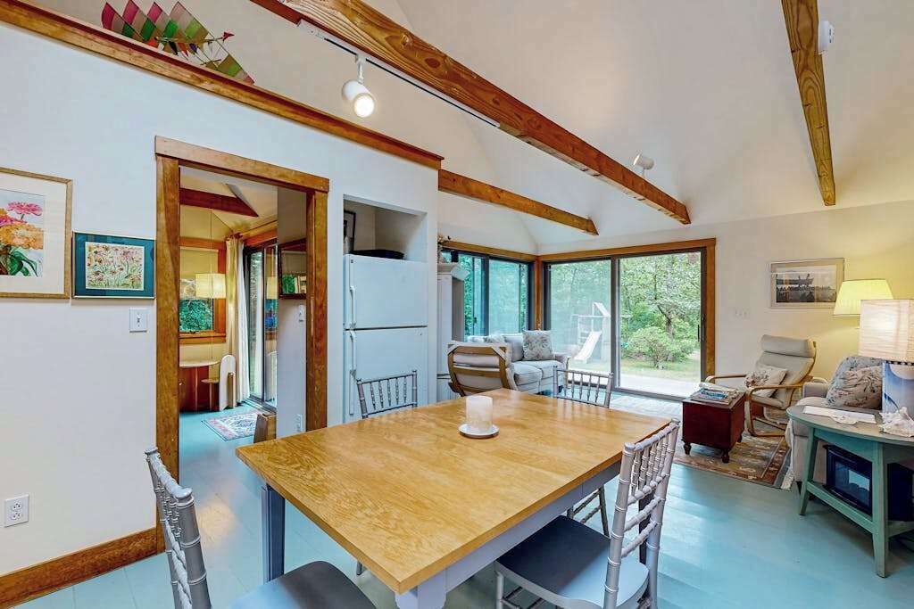 Une pièce spacieuse comprenant une table à manger en bois, des chaises, un canapé et une grande fenêtre donnant sur un paysage verdoyant.