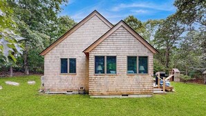 A two-story wooden cabin with a sloped roof, a small porch, and a fenced yard.
