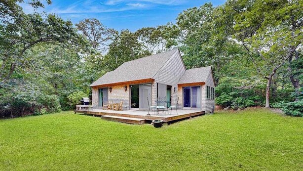A single-story house with a deck, surrounded by a well-maintained lawn and trees.