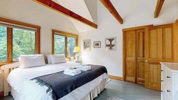 Une chambre à coucher avec un lit, des tables de chevet, une lampe, des tableaux encadrés, une armoire en bois et de grandes fenêtres.