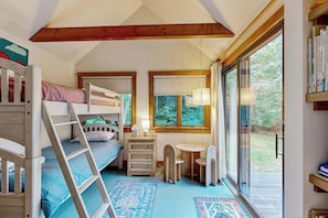 A cozy bedroom with bunk beds, a desk, and a window with a view of greenery.