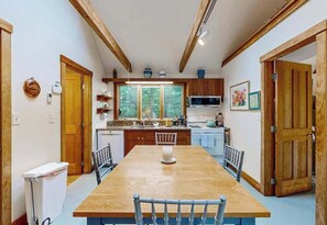 A kitchen with wooden beams, a dining table, chairs, and a view of the outdoors.