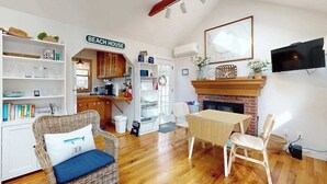 A cozy living room with a dining area, a fireplace, and a kitchen in the background. - Cottage near Cape Cod National Seashore with firepit, grill, kitchenette, & AC (Eastham)