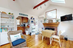 A cozy living room with a dining area, a fireplace, and a kitchen in the background. - Cottage near Cape Cod National Seashore with firepit, grill, kitchenette, & AC (Eastham)