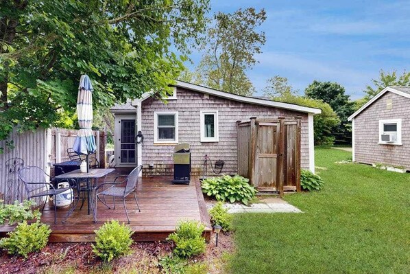 A single-story house with a deck, a small porch, and a fenced backyard. - Cottage near Cape Cod National Seashore with firepit, grill, kitchenette, & AC (Eastham)