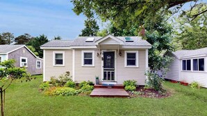 A single-story house with a front porch, a small garden, and a visible garage door. - Cottage near Cape Cod National Seashore with firepit, grill, kitchenette, & AC (Eastham)