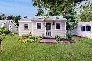 A single-story house with a front porch, a small garden, and a visible garage door. - Cottage near Cape Cod National Seashore with firepit, grill, kitchenette, & AC (Eastham)
