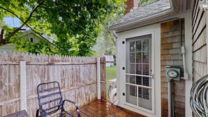 A wooden deck with a metal chair, a small door with a window, and a utility box. - Cottage near Cape Cod National Seashore with firepit, grill, kitchenette, & AC (Eastham)