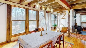 Ein rustikales Holzinnenzimmer mit Esstisch, Stühlen, großen Fenstern und einem Kamin.