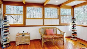 Ein gemütliches Zimmer mit Holzboden, einem Korbstuhl mit Kissen, einem kleinen Holzschrank und einem hohen Bücherregal.