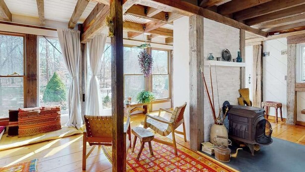 Ein rustikales Interieur mit Holzboden, einer Couch, einem Sessel, einem Tisch, einem Kamin und einem Fenster mit Blick auf Bäume.