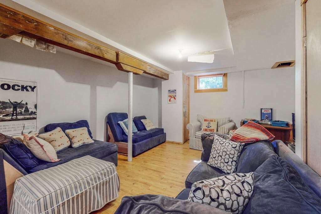 A living room with a blue sofa, a striped ottoman, and a wooden ceiling beam.