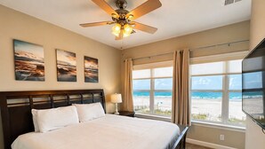 Ein Schlafzimmer mit Bett, Deckenventilator, Nachttisch, Lampe und Blick auf den Strand.