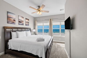 Ein Hotelzimmer mit Bett, Deckenventilator, Fernseher und Blick auf den Strand.