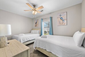 A hotel room with two beds, a ceiling fan, artwork on the walls, and a window with curtains. - Gulf Front | 6 Bedrooms | Spacious West Beach Retreat (Gulf Shores)