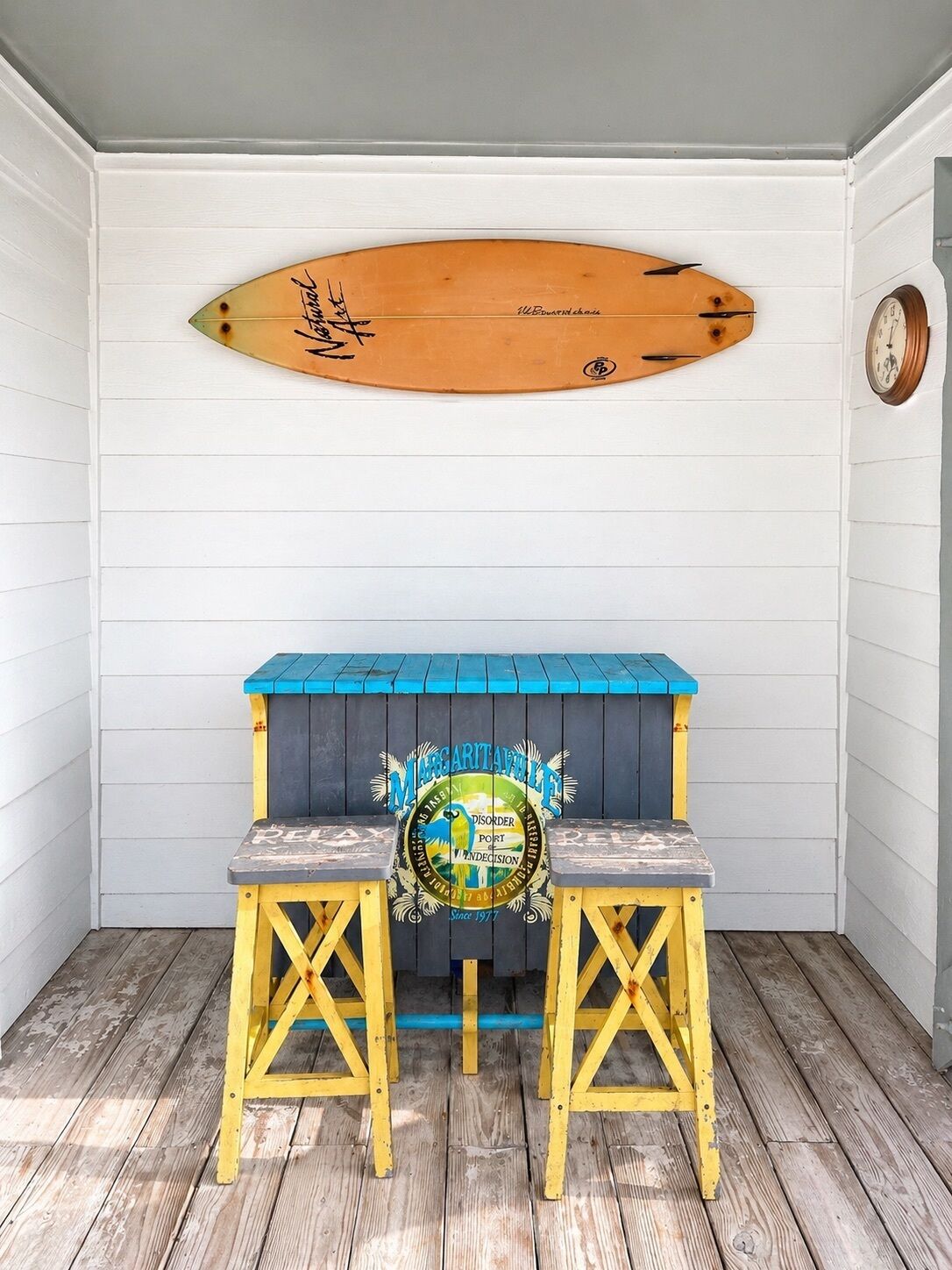 A wooden surfboard with signatures, a blue and yellow bench with a logo, and a clock on the wall.