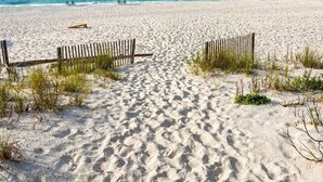 Ein sandiger Strand mit einem hölzernen Weg zum Wasser, einem klaren Himmel und einem ruhigen Meer.
