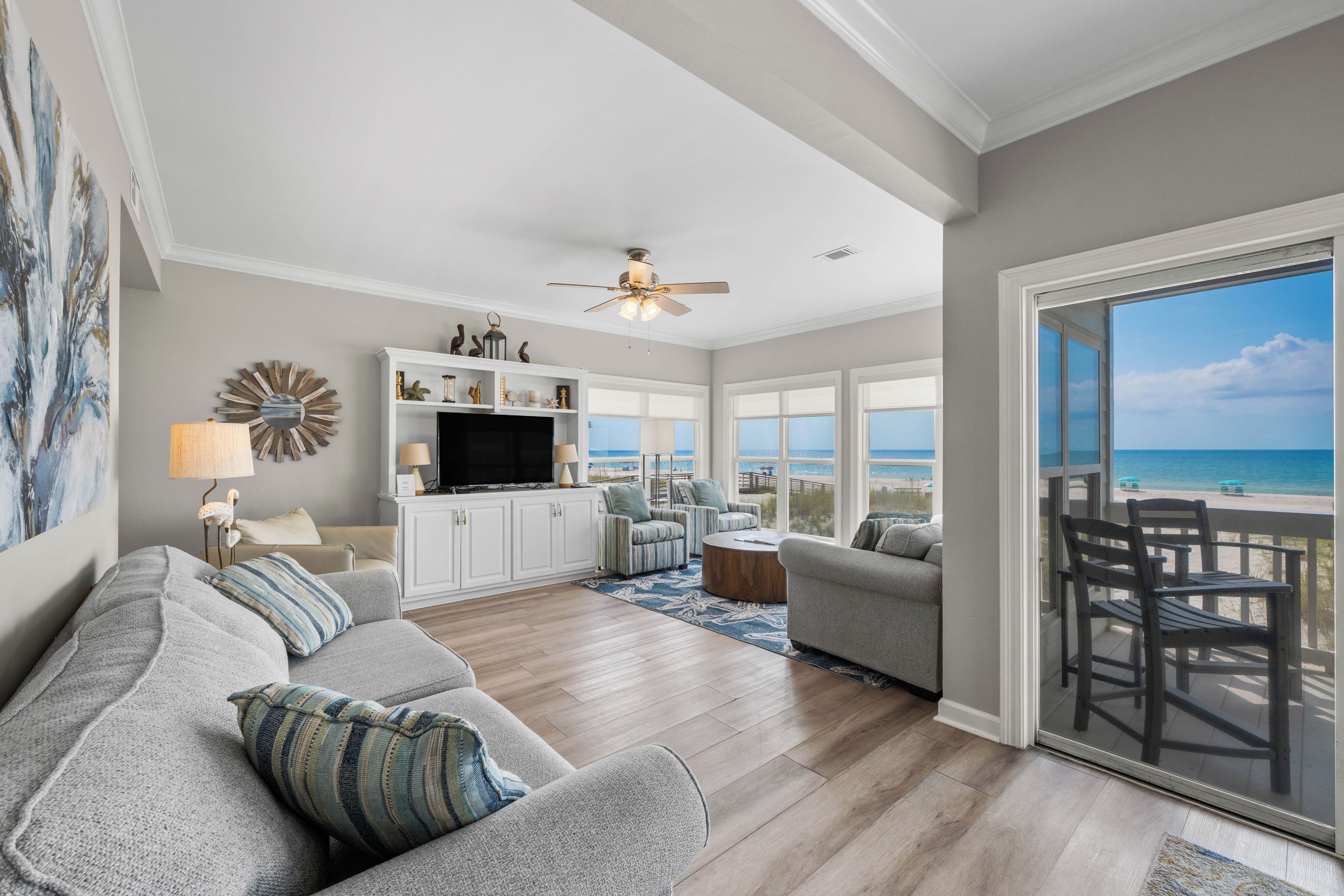 A spacious living room with a large sofa, a television, and a view of the beach through the sliding glass door.