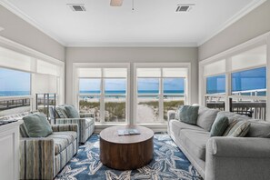 Ein geräumiges Wohnzimmer mit großem Fenster mit Blick auf einen Strand, einem runden Couchtisch und zwei Sofas.