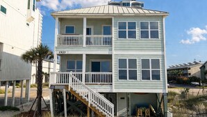 Ein zweistöckiges Strandhaus mit Balkon, einer Treppe und einem Sandstrand im Vordergrund.