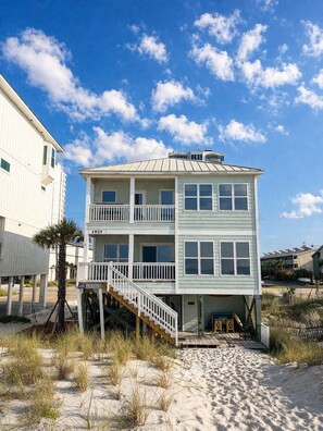 A two-story beach house with a balcony, a staircase, and a sandy beach in the foreground. - Gulf Front | 6 Bedrooms | Spacious West Beach Retreat (Gulf Shores)