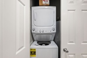 A compact washer and dryer unit in a small laundry room with a door handle and a yellow energy guide sticker. - Gulf Front | 6 Bedrooms | Spacious West Beach Retreat (Gulf Shores)
