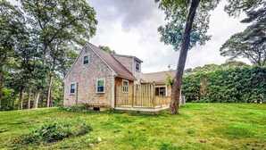 Ein eingeschossiges Holzhaus mit einer Veranda, umgeben von einem Rasen und Bäumen.