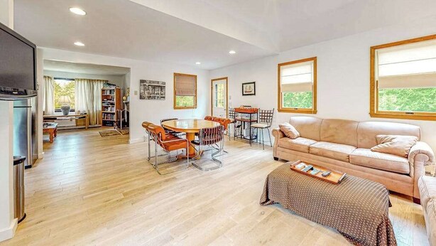Ein geräumiger Wohnbereich mit Holzboden, einem beigefarbenen Sofa, einem Esstisch mit Stühlen und einer Küchenzeile mit Kühlschrank.