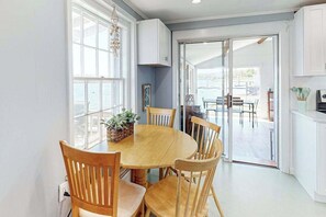 A dining area with a round table, wooden chairs, a potted plant, and a view through glass doors to an outdoor patio. - Historic charmer on the water with a firepit, kayaks, bikes, & firepit (Eastham)