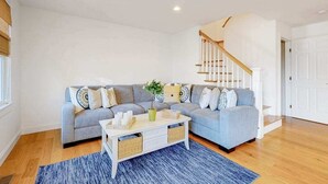 Ein Wohnzimmer mit grauem Sofa, weißem Couchtisch, blauem Teppich und einer Treppe.