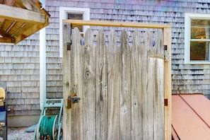 A wooden fence with a metal latch, a green hose reel, and a wooden structure to the left.