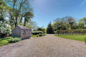 A gravel driveway leading to a wooden structure, surrounded by greenery and trees.