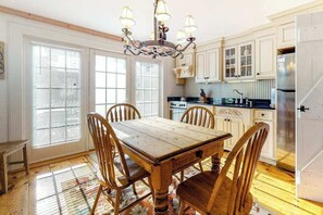 A kitchen with a wooden table, chairs, a chandelier, and white cabinets.