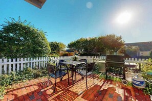 A patio with a grill, outdoor seating, and a white picket fence.