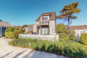 A two-story house with a white picket fence, a driveway, and a large tree.
