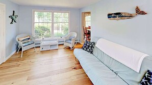 Et værelse med en lyseblå væg, en hvid sofa, en hvid stol, et lille bord og et vindue med udsigt over grønne områder.