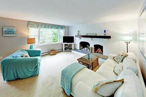 Ein Wohnzimmer mit Kamin, einer Couch, einem Fernseher und einem Fenster mit Vorhängen.