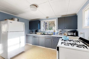 A kitchen with a white refrigerator, grey cabinets, a stove, and a window. - Dog-Friendly Downtown Home w/Free WiFi, Deck, Water Views, & Partial A/C (Oak Bluffs)