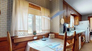 A cozy kitchen with wooden cabinets, a dining table with a placemat, and a window with curtains. - Cozy Cape style home near the beach and ferry with patio, W/D, & AC (Hyannis)
