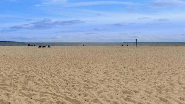 A wide sandy beach with footprints, a few people, and a distant shoreline. - Cozy Cape style home near the beach and ferry with patio, W/D, & AC (Hyannis)